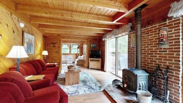 A log cabin interior with a fireplace, red sofas, wooden floors, and a television.