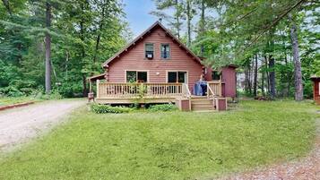 A cabin with a wooden deck, a small porch, and a fenced yard.