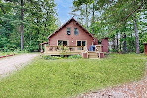 Eine Holzhütte mit einer Holzterrasse, einer kleinen Veranda und einem umzäunten Garten.