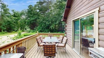 A wooden deck with a table and chairs, surrounded by a wooden railing, overlooking a forested area.