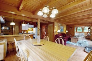 Ein Interieur einer Holzhütte mit einem Esstisch, Stühlen, einer Couch und einer Küchenzeile.