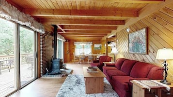 A wooden interior with a fireplace, a sofa, a dining table, and a large window.