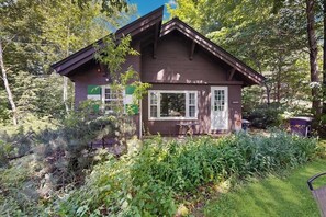 A small, single-story cabin with a pitched roof, surrounded by dense greenery and trees. - Dog-friendly & charming mountain chalet w/ fireplace (Franconia)