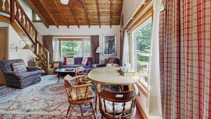 Techo de madera, una mesa de comedor, un sofá y una ventana con cortinas.