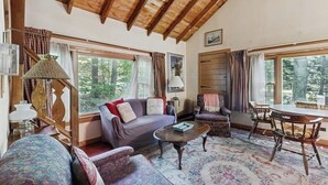 Una habitación acogedora con techo de madera, un sofá, una silla, una mesa y una ventana con cortinas.