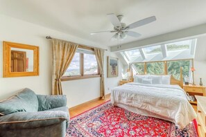Une chambre à coucher avec un lit, un ventilateur de plafond, une fenêtre avec des rideaux, une porte en bois et un canapé bleu.
