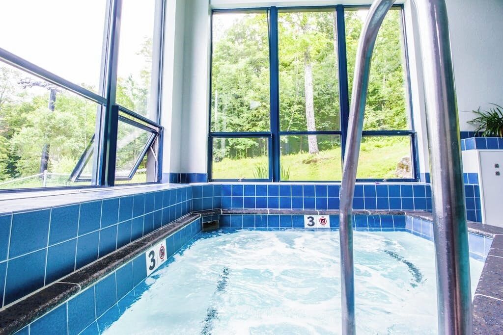 Un bain à remous avec vue sur une forêt, un panneau portant le chiffre 3 et une échelle en métal.
