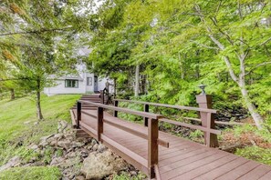 Un pont en bois mène à un bâtiment blanc, lui-même entouré d’une végétation luxuriante.