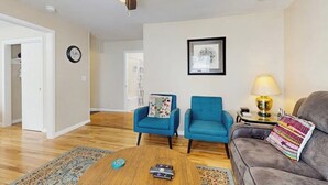 Ein Wohnzimmer mit Deckenventilator, einem blauen Sessel, einem grauen Sofa, einem Couchtisch und einer Lampe.