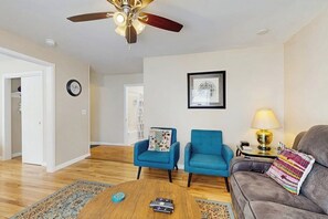 A living room with a ceiling fan, a blue armchair, a grey sofa, a coffee table, and a lamp.