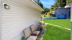Ein Wohnhaus mit einer Terrasse, die einen Grill, Stühle und einen Tisch bietet.