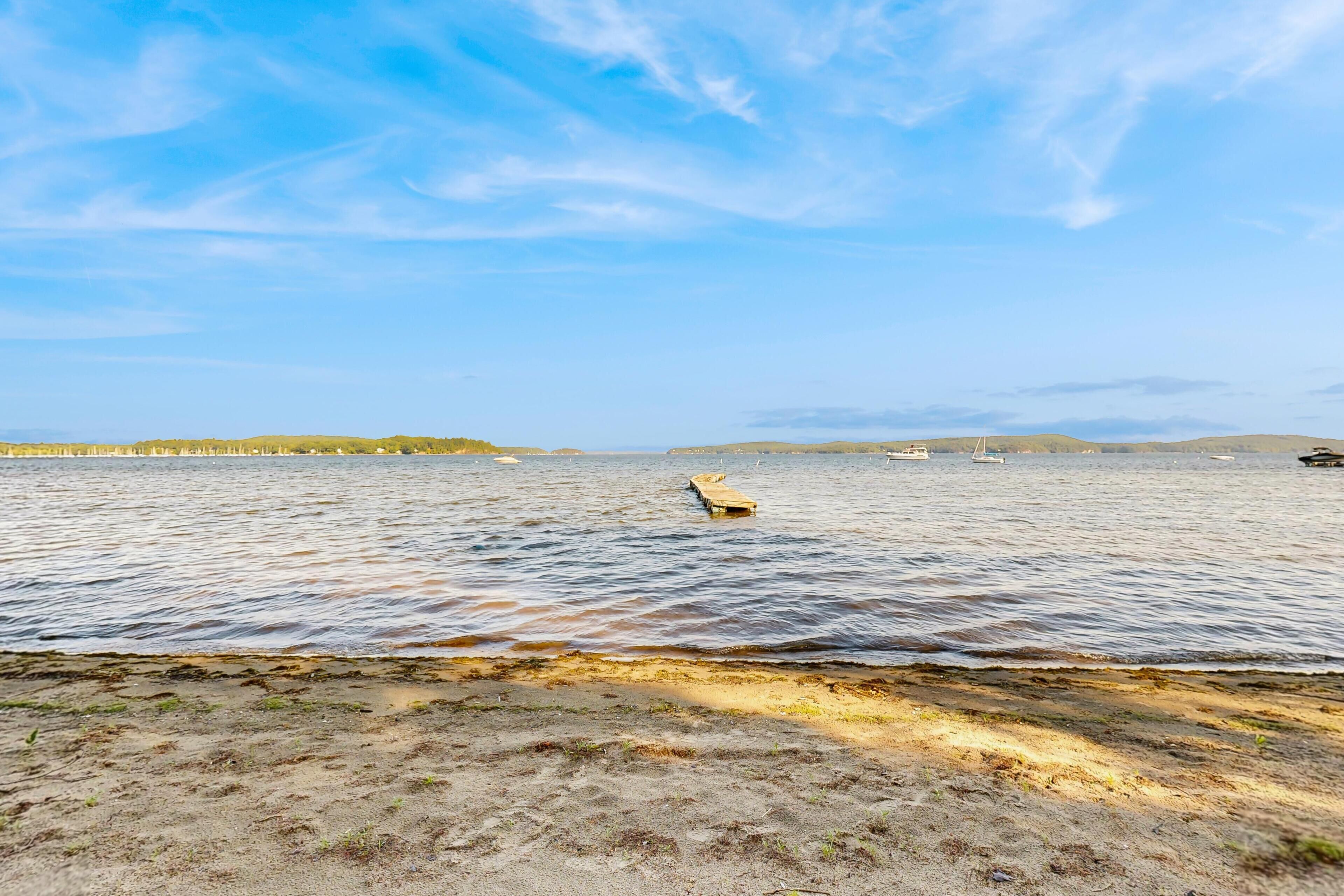A coastal landscape with a sandy beach, calm water, and distant hills.