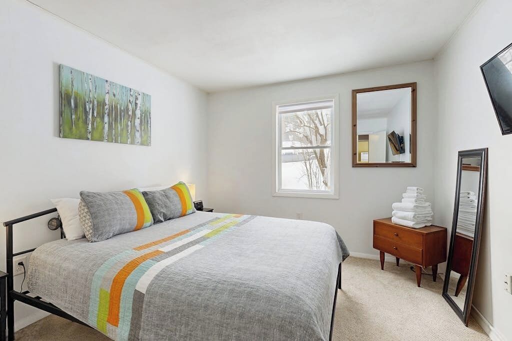 A bedroom with a bed, a window, a dresser, and a mirror.