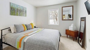 Ein Schlafzimmer mit Bett, Fenster, Kommode und Spiegel.