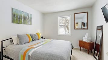 A bedroom with a bed, a window, a dresser, and a mirror.