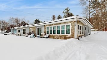 A two-story house with a stone facade, large windows, and a snow-covered yard.
