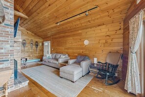 A log cabin interior with a wooden ceiling, a fireplace, a sofa set, a rocking chair, and a patterned rug. - Summer Fun, Lake View, Firepit, Outdoor grilling, walk to the lake (Naples)