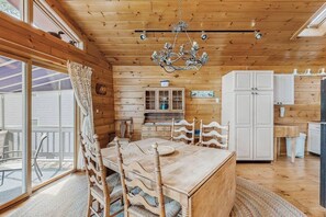 A wooden cabin interior with a dining table, chairs, a chandelier, cabinets, and a sliding glass door to the outside. - Summer Fun, Lake View, Firepit, Outdoor grilling, walk to the lake (Naples)