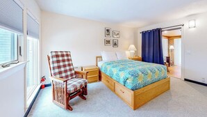 Ein Schlafzimmer mit einem Bett, einem Sessel, einem Nachttisch, einer Lampe und einem Fenster mit Jalousien.