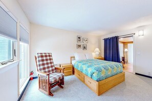 Une chambre à coucher comprenant un lit, une chaise, une table de chevet, une lampe et une fenêtre avec des stores.