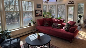 A sunlit living room with a red sofa, multiple windows, and indoor plants.