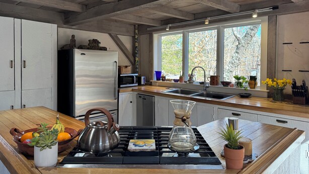 A modern kitchen with a wooden countertop, stainless steel appliances, and a window with a view of trees.