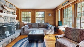 Ein gemütliches Wohnzimmer mit Kamin aus Stein, einer Eckcouch und einem gestreiften Sessel.