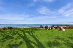 A grassy outdoor area with chairs and a stone structure, overlooking a body of water. - Charming oceanfront house with incredible beach views, BBQ area & firepit (York)