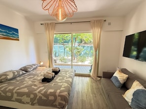 Ein Schlafzimmer mit Bett, einer Couch, einem Fernseher und Blick auf einen Garten.