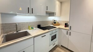 A modern kitchen with white cabinets, a stainless steel sink, a built-in oven, and a black induction cooktop. - Terrasse & Calme • 8 min mer • Garage privé (Antibes)