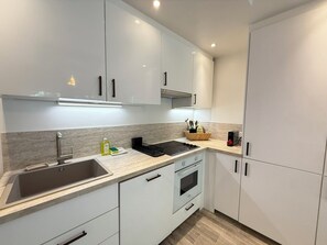 Eine moderne Küche mit weißen Schränken, einer Edelstahl-Spüle, einem eingebauten Backofen und einer schwarzen Induktionskochplatte.
