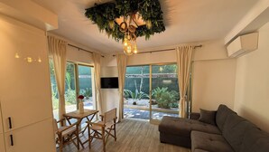 A modern living room with a wooden floor, a brown sofa, a dining table with chairs, and a TV. - Terrasse & Calme • 8 min mer • Garage privé (Antibes)