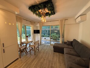 Ein modernes Wohnzimmer mit Holzboden, einem braunen Sofa, einem Esstisch mit Stühlen und einem Fernseher.