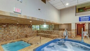 Een binnenzwembad met een jacuzzi, betegelde muren en een vluchtwegbord.