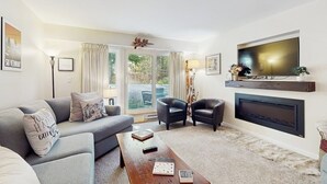 Een woonkamer met een bank, twee fauteuils, een salontafel met boeken, een open haard en een televisie.