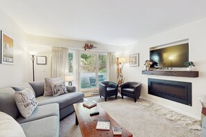 Ein Wohnzimmer mit einer Couch, zwei Sesseln, einem Couchtisch mit Büchern, einem Kamin und einem Fernseher.
