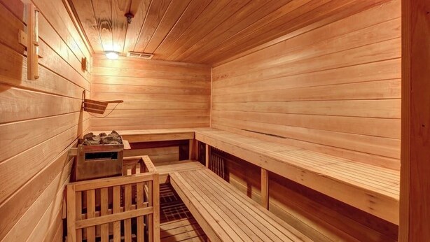 Een houten sauna met banken en een zitting, een houten vloer, en een lamp aan het plafond.