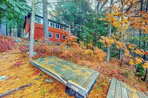 Une cabane à l’extérieur rouge, entourée d’une forêt aux couleurs automnales.