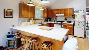 Une cuisine moderne avec des meubles en bois, un grand îlot central doté de tabourets, un four à micro-ondes, une cuisinière et un réfrigérateur.