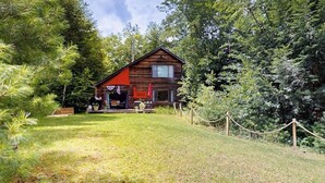 Une cabane avec un toit rouge, entourée d’une zone herbeuse et d’une forêt dense.