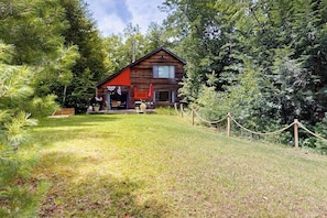 Eine Hütte mit rotem Dach, umgeben von einer grünen Wiese und dichtem Baumbestand.