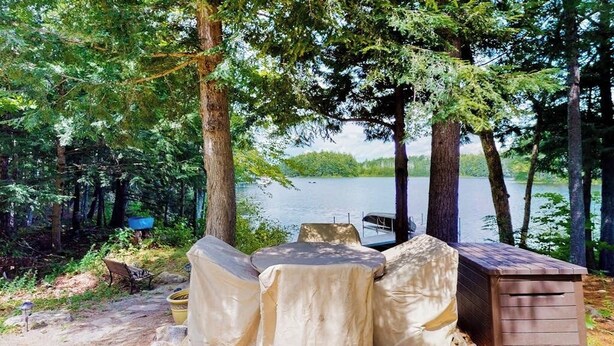 Un espace extérieur abrité, aménagé avec des sièges, offrant une vue sur un lac et entouré d’arbres.