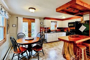 A kitchen with a wooden island, white cabinets, and a dining area with a round table and chairs. - Immaculate All-Season Retreat with Must-See Game Room! (Bethel)