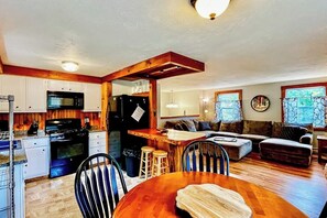 A kitchen with a microwave, stove, and refrigerator, a dining area with a wooden table and chairs, and a living room with a sofa and a coffee table. - Immaculate All-Season Retreat with Must-See Game Room! (Bethel)