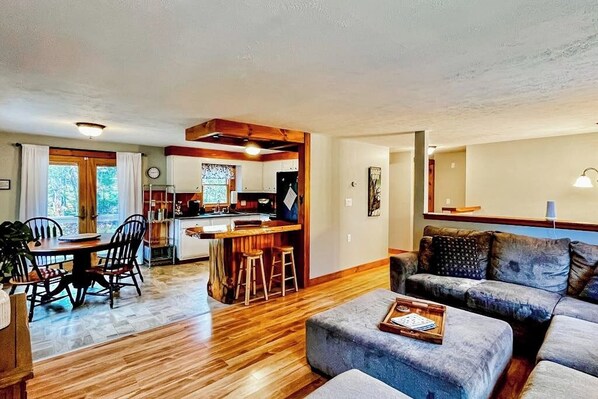 A living room with a sofa, ottoman, and dining area with chairs and a table. - Immaculate All-Season Retreat with Must-See Game Room! (Bethel)