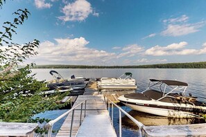 A dock with several boats, a wooden pier, and a calm lake with trees in the background.
