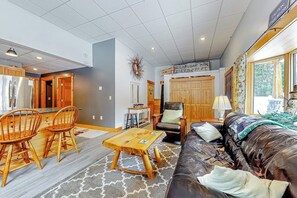 A living room with a sofa, chairs, a coffee table, and a kitchen area with cabinets and a refrigerator. - Cozy, ground-floor duplex retreat with direct shuttle service to Sugarloaf (Carrabassett Valley)