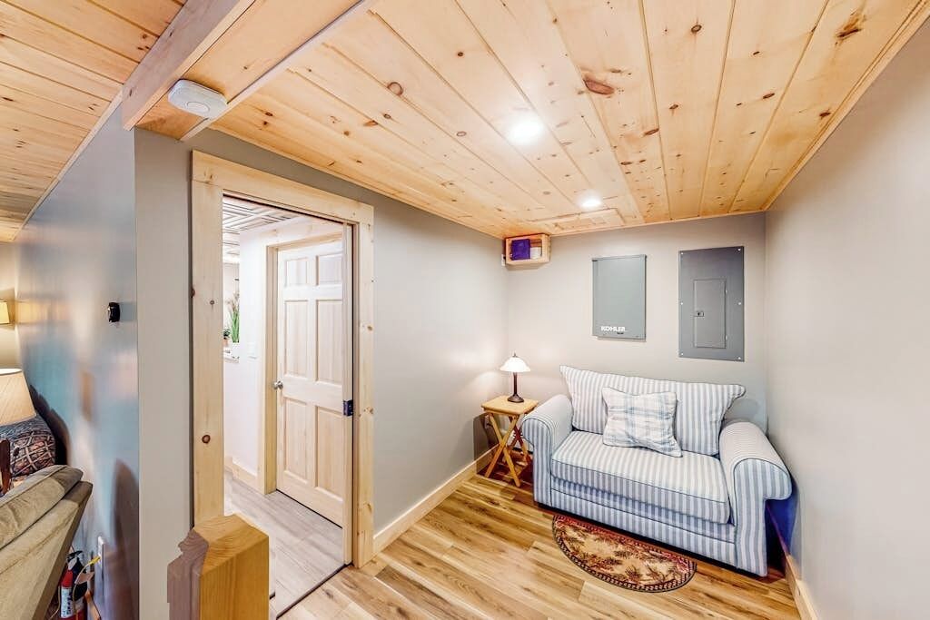 Een kamer met een houten plafond, een gestreept sofa, een klein bijzettafeltje en een deur naar buiten.