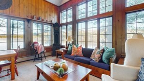 A cozy living room with a wooden interior, large windows, a sofa, a coffee table, and a fireplace. - Tranquil Lakefront Retreat with large outdoor patio, beach and Stunning Views (Denmark)