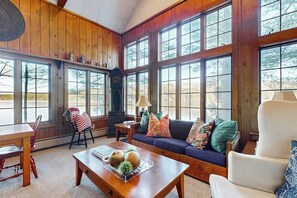 A cozy living room with a wooden interior, large windows, a sofa, a coffee table, and a fireplace.